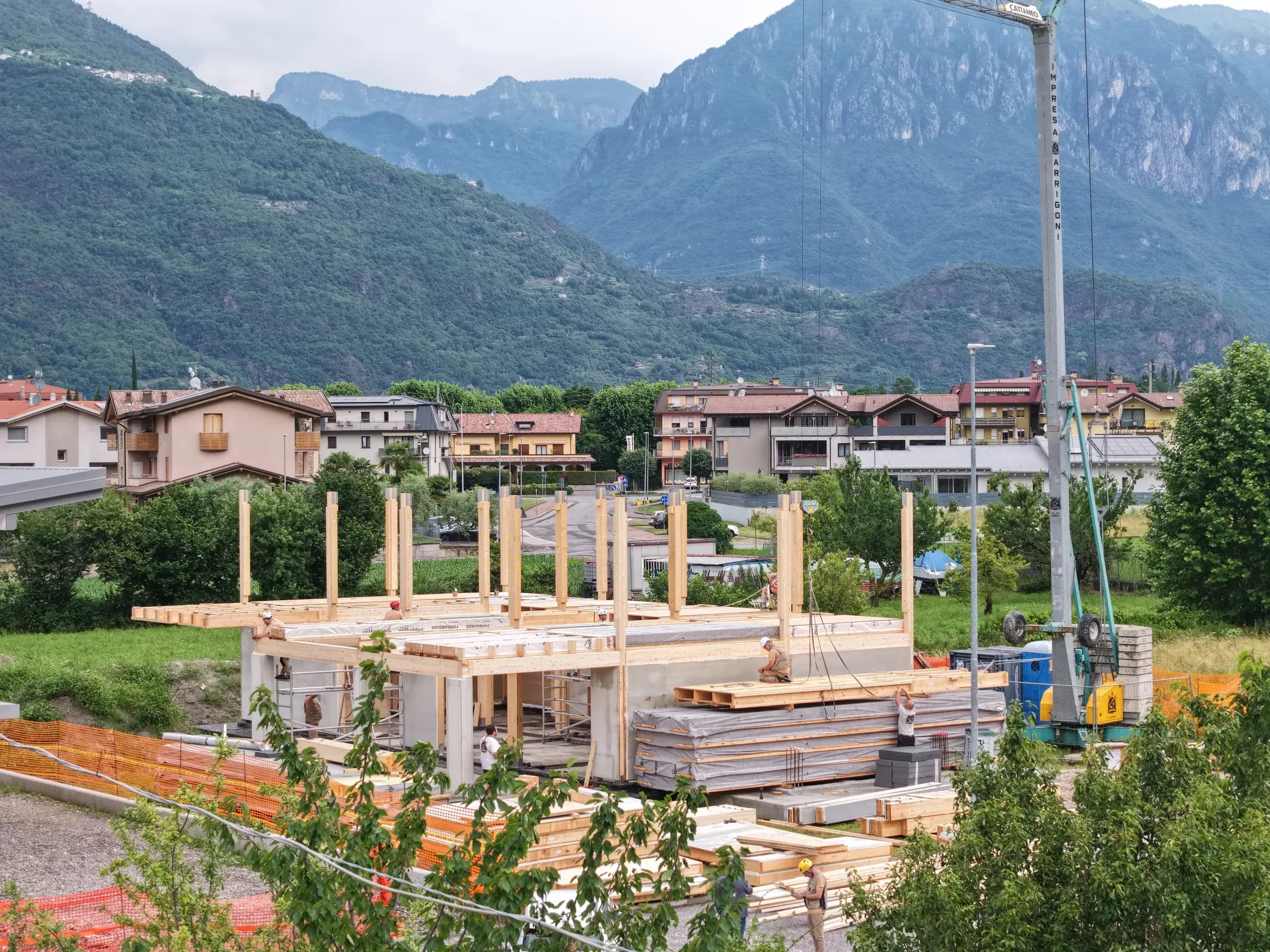 Cantiere della residenza X-Frame di Brescia in contesto prealpino, con gru di montaggio e pacchi di elementi costruttivi